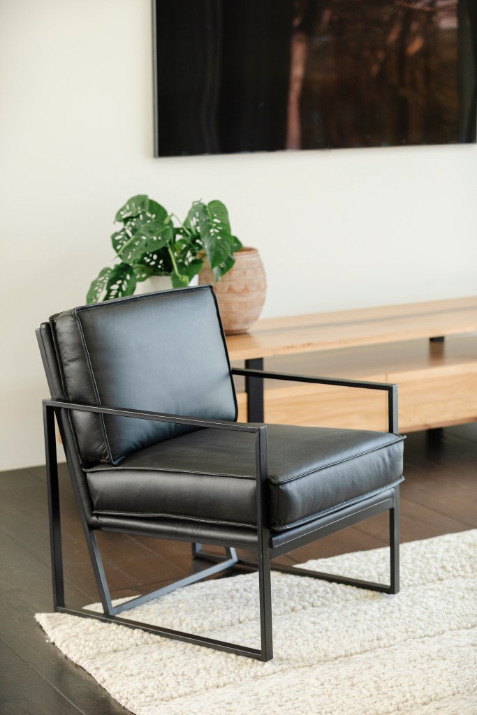 Black, leather armchair resting on rug, with wall-mounted TV in and greenery in the background.